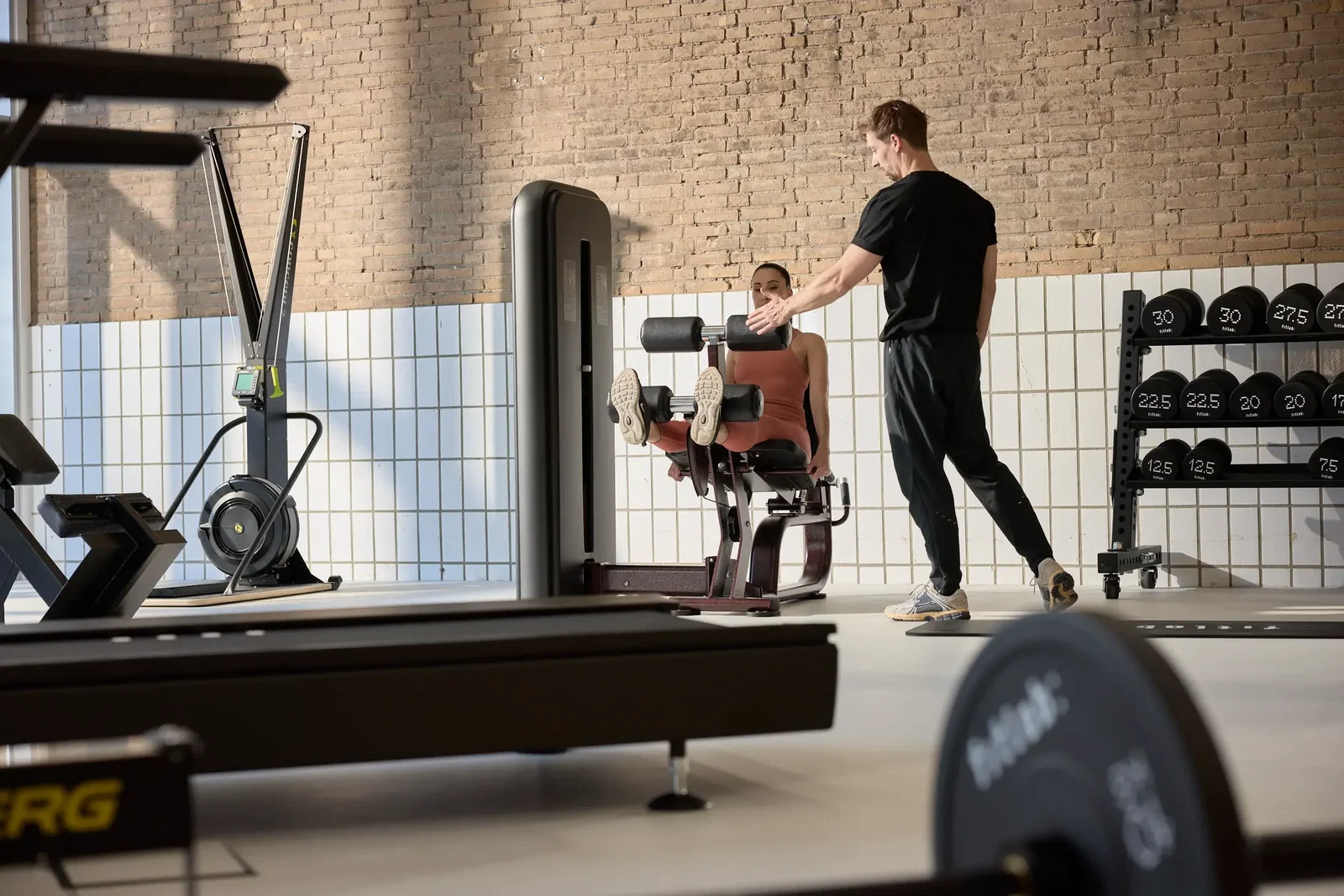 Een personal trainer begeleidt een klant op een trainingstoestel in de Fitlab-studio.
